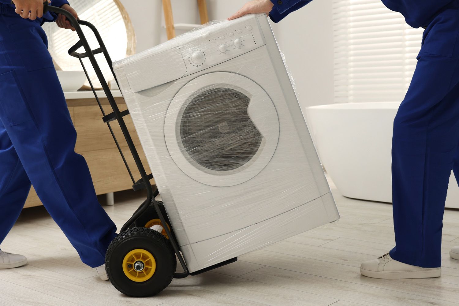Två personer från en flyttfirma bär ut en tvättmaskin.